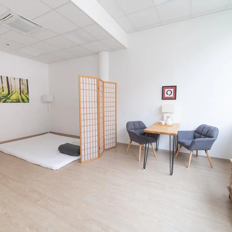 Cozy consultation corner with two grey armchairs, a wooden table, lamp and a zen circle artwork.