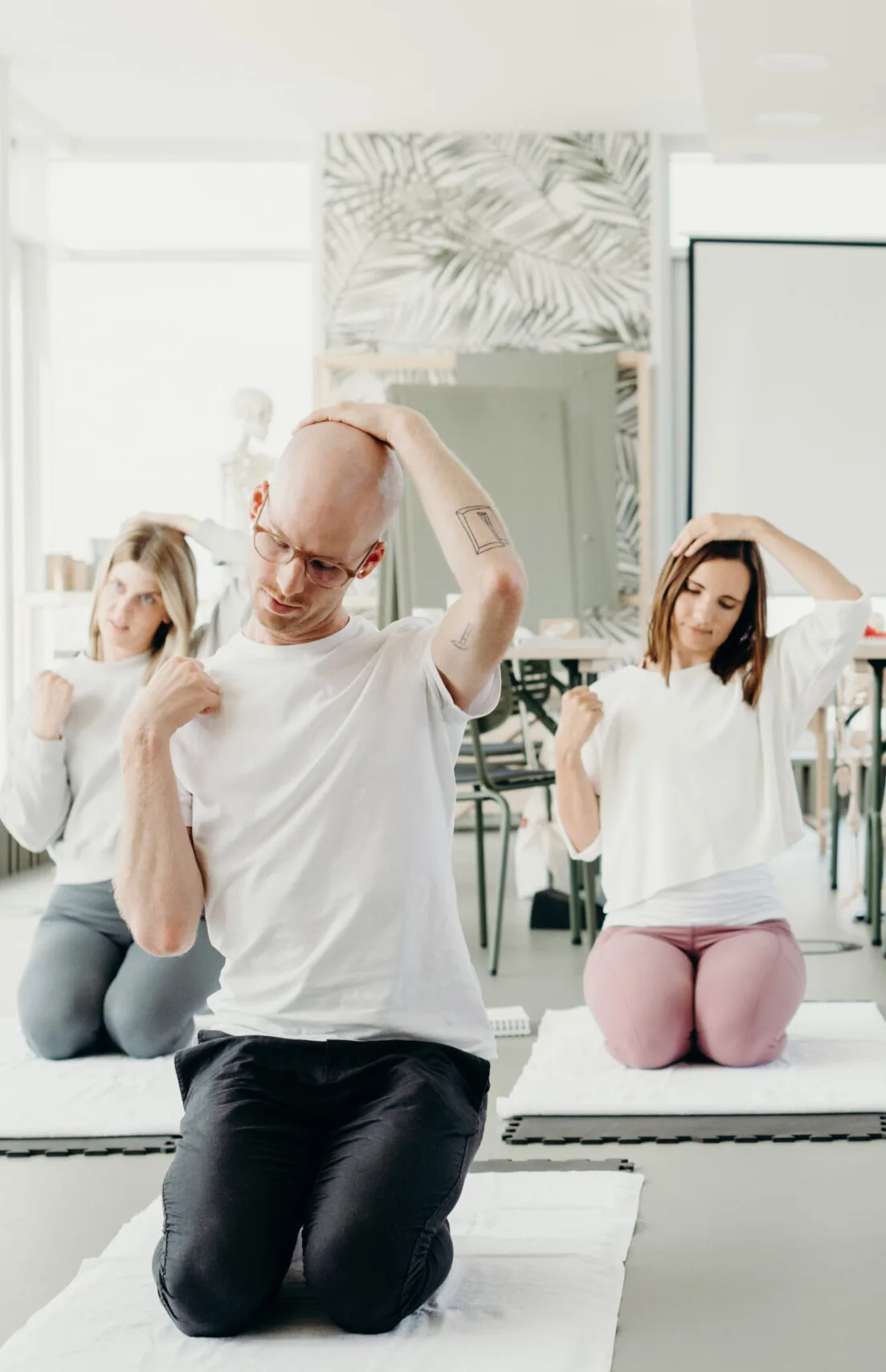A group stretching class with participants kneeling and doing neck stretches guided by an instructor.