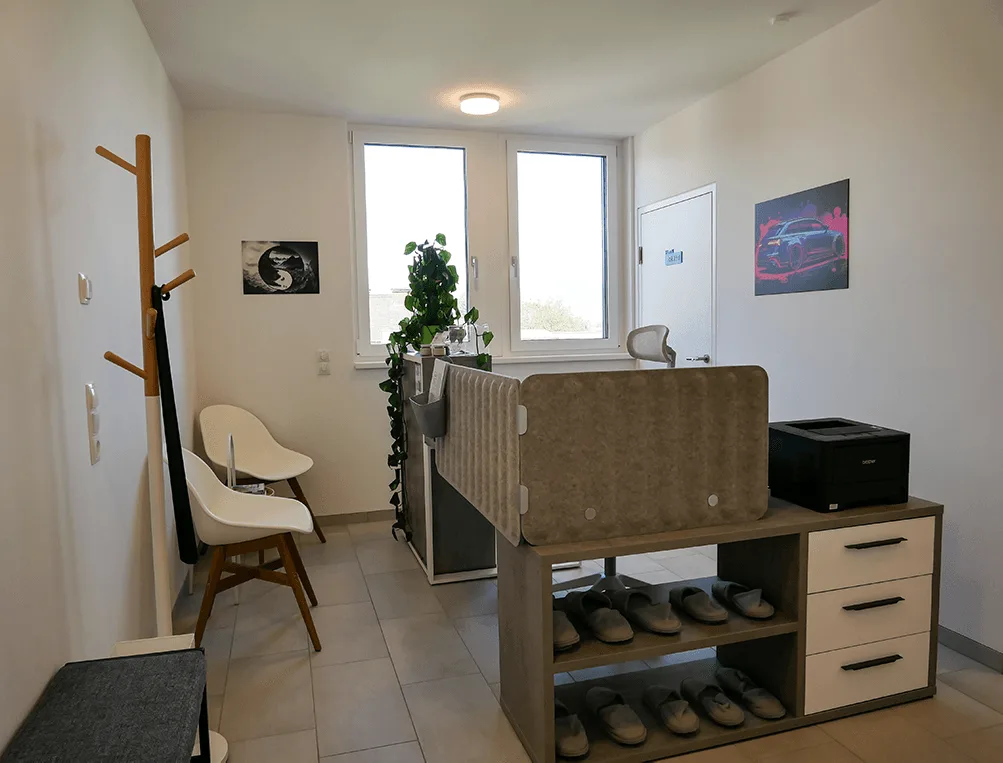 A modern reception and waiting area with white chairs, plants, a desk, and motivational wall art.