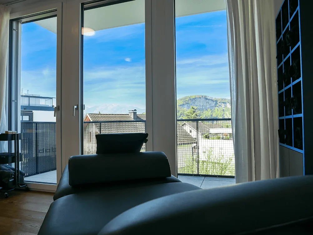 A therapy treatment table in the foreground with a panoramic balcony view of mountains and blue sky.