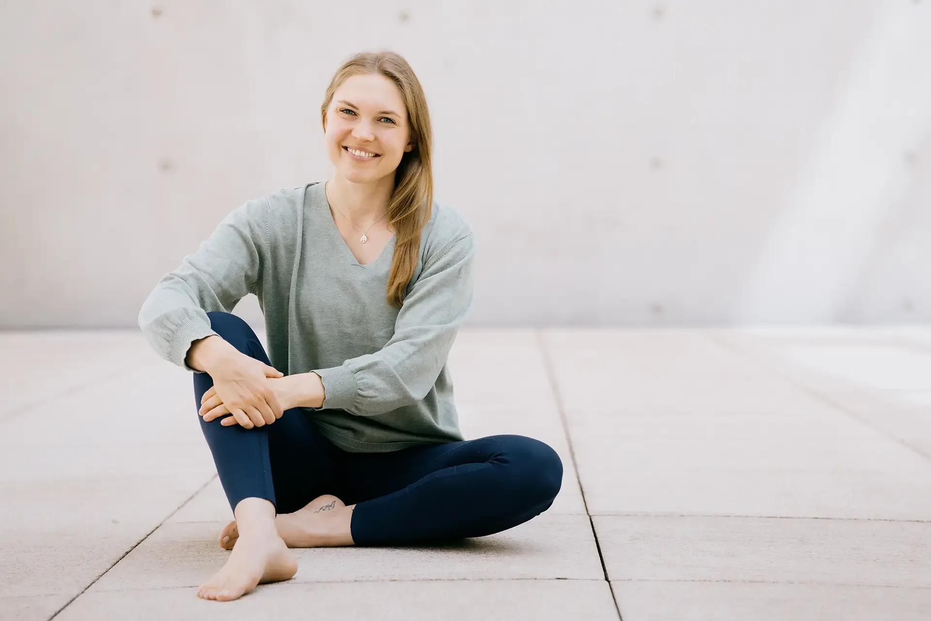 A woman performs a graceful yoga lunge pose outdoors, arms raised high against a minimal concrete background.