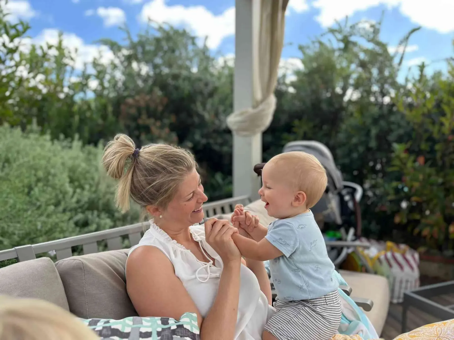 Smiling blonde mother playing joyfully with her baby on an outdoor terrace, reflecting the happy results of successful breastfeeding support.